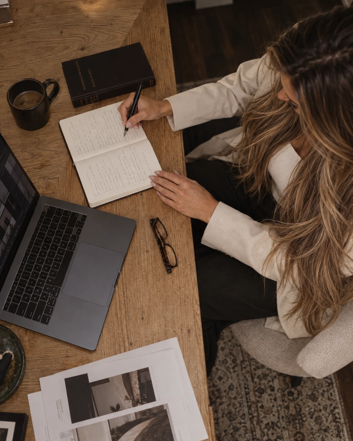Chloe writing in a notebook beside a MacBook at a wooden desk